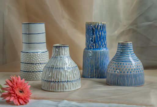 Four Blue and White handmade ceramic vase with Pink flower on Blush textured table cloth. Home decor, Copy space, Selective focus.