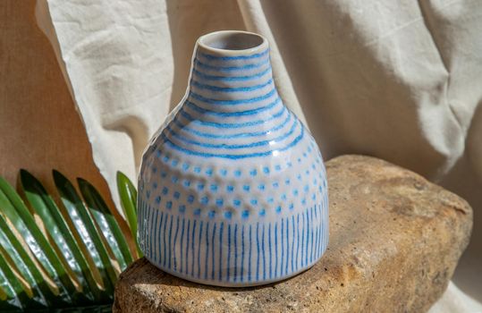 White and Blue handmade ceramic vase on white textured table cloth.  Home decor, Copy space, Selective focus.