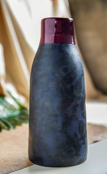 Blue and Crimson  handmade ceramic vase on white textured table cloth.  Home decor, Copy space, Selective focus.