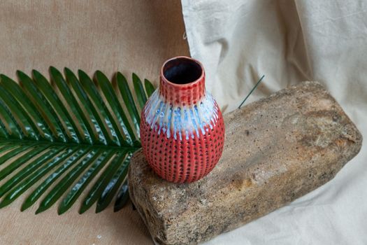 Red handmade ceramic vase on white textured table cloth.  Home decor, Copy space, Selective focus.