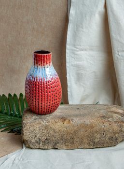 Red handmade ceramic vase on white textured table cloth.  Home decor, Copy space, Selective focus.