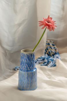 Pink flower in Blue handmade ceramic vase on Blush textured table cloth. Home decor, Copy space, Selective focus.