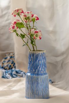 Bouquet of flower in Blue handmade ceramic vase on Blush textured table cloth. Home decor, Copy space, Selective focus.