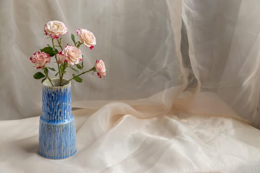 Bouquet of flower in Blue handmade ceramic vase on Blush textured table cloth. Home decor, Copy space, Selective focus.