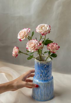 Hands of a young woman with Blue handmade ceramic vase and Bouquet of flower on Blush textured table cloth. Home decor, Copy space, Selective focus.