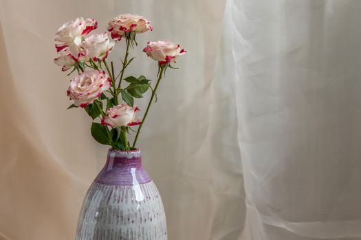 Close-up of Bouquet of flower in Purple and White handmade ceramic vase on Blush textured table cloth. Home decor, Copy space, Selective focus.