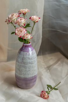 Bouquet of flower in Purple and White handmade ceramic vase on Blush textured table cloth. Home decor, Copy space, Selective focus.