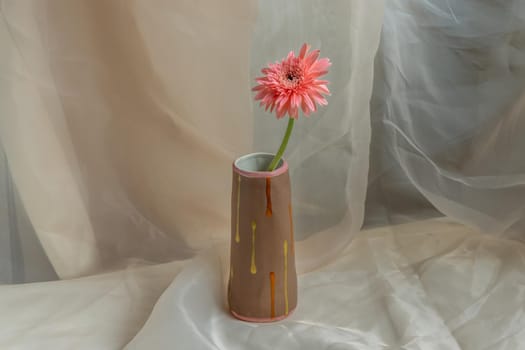 Pink flower in Brown handmade ceramic vase on Blush textured table cloth. Home decor, Copy space, Selective focus.