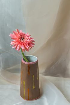 Pink flower in Brown handmade ceramic vase on Blush textured table cloth. Home decor, Copy space, Selective focus.