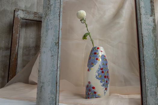 White flower in Blue and White, Red, Yellow handmade ceramic vase on Blush textured table cloth. Home decor, Copy space, Selective focus.