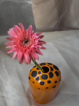 Pink flower in Orange handmade ceramic vase on Blush textured table cloth. Home decor, Copy space, Selective focus.
