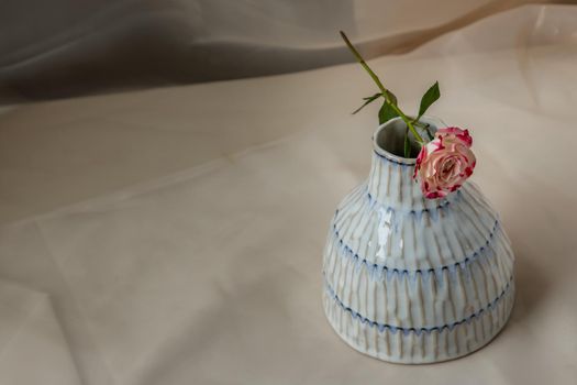Rose flower on Copper color handmade ceramic vase and on Blush textured table cloth. Home decor, Copy space, Selective focus.