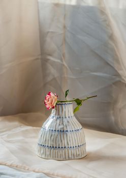 Rose flower on Copper color handmade ceramic vase and on Blush textured table cloth. Home decor, Copy space, Selective focus.