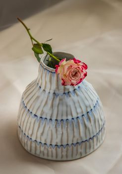 Rose flower on Copper color handmade ceramic vase and on Blush textured table cloth. Home decor, Copy space, Selective focus.