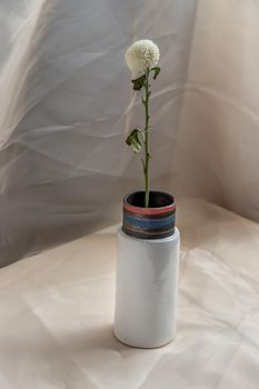 White flower in White handmade ceramic vase and on Blush textured table cloth. Home decor, Copy space, Selective focus.
