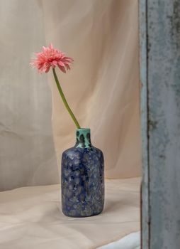 Pink flower in Blue handmade ceramic vase on Blush textured table cloth. Home decor, Copy space, Selective focus.