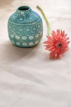 Blue handmade ceramic vase with Pink flower on Blush textured table cloth. Home decor, Copy space, Selective focus.
