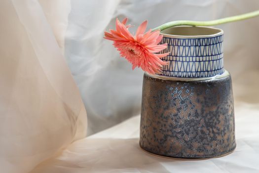 Pink flower on Blue handmade ceramic vase and on Blush textured table cloth. Home decor, Copy space, Selective focus.