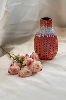 Red vase with Bouquet of flowers on Blush textured table cloth. Home decor, Copy space, Selective focus.