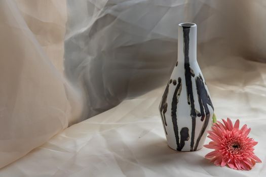 Black and White handmade ceramic vase with Pink flower on Blush textured table cloth. Home decor, Copy space, Selective focus.