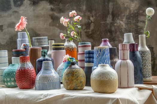 Bouquet of flowers in Handmade Assorted Many Different Ceramic Vases on Calico textured table cloth with old cement wall. Home decor. Selective focus.