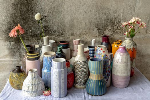 Bouquet of flowers in Handmade Assorted Many Different Ceramic Vases on Calico textured table cloth with old cement wall. Home decor. Selective focus.