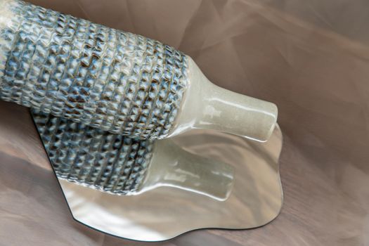 Handmade ceramic vase bottle shape on mirror on fabric textured table cloth. Home decor, Copy space, Selective focus.
