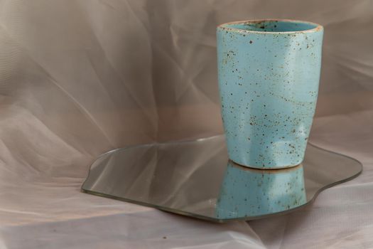 Blue handmade ceramic mug on mirror on fabric textured table cloth. Home decor, Copy space, Selective focus.