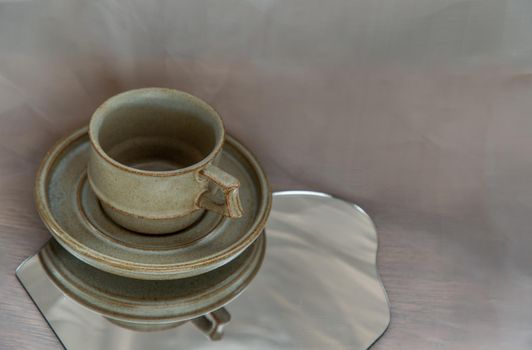 Handmade ceramic coffee mug on mirror on fabric textured table cloth. Home decor, Copy space, Selective focus.