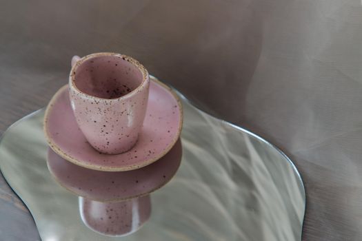 Pink handmade ceramic mug on mirror on fabric textured table cloth. Home decor, Copy space, Selective focus.