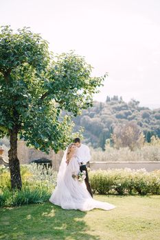 The bride and groom in the shade of a tree. The wedding couple walks in the garden. Wedding in Florence, Italy, in an old villa-winery.