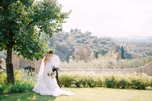 The bride and groom in the shade of a tree. The wedding couple walks in the garden. Wedding in Florence, Italy, in an old villa-winery.