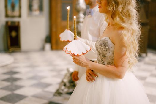 The bride and groom stand with candles in their hands at the altar in the church of St. Nicholas in Kotor during the wedding . High quality photo