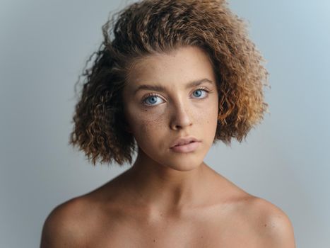 Beautiful woman portrait light background bared shoulders curly hair. High quality photo