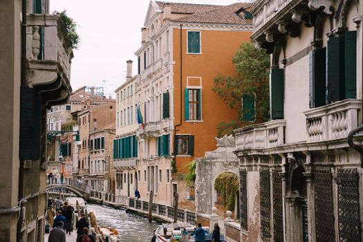 A classic view of the narrow sea Venetian canal. Colorful buildings stand opposite each other, boats moored near the shore, gondolier rides tourists on a gondola. Blue skies on a sunny day.