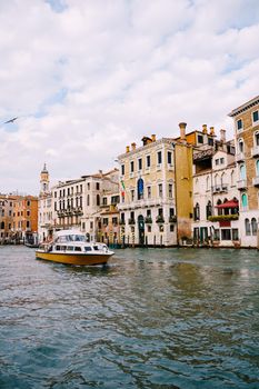 Tourists on the waterfront in Venice, against the background of the ancient facades of buildings standing in water. Water sightseeing in Venice, Italy.