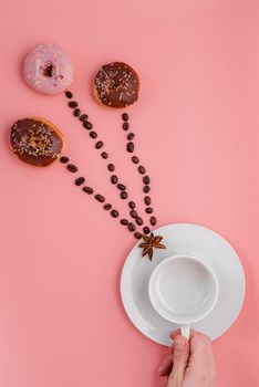 hand holding empty cup, beans and three doughnut on pink background