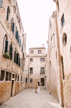 The bride and groom walk through the deserted streets of the city. Newlyweds walk in a dead-end alley against the background of brick buildings.