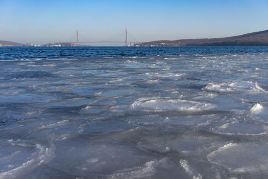 The sea surface covered with ice and the Russian bridge on the horizon.Vladivostok, Russia