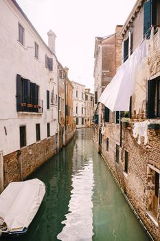 Beautiful narrow canal in Venice, Italy. Small stone bridge connects houses from both sides of the canal. Building facades are aged by weather and water.