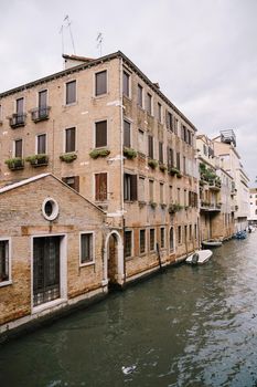 Boats moored at the walls of a building in canal in Venice, Italy. Classic Venetian street views - wooden shutters, brick houses, bridges