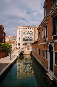Beautiful narrow canal in Venice, Italy. Small stone bridge connects houses from both sides of the canal. Building facades are aged by weather and water.