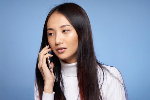 Asian woman talking on a cell phone on a blue background. High quality photo