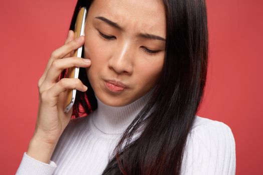 sad asian woman talking on the phone close-up red background. High quality photo