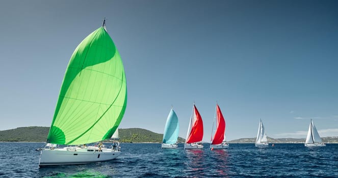 Sailboats compete in a sail regatta at sunset, race of sailboats, reflection of sails on water, multicolored spinnakers, number of boat is on aft boats, big white clouds is on background