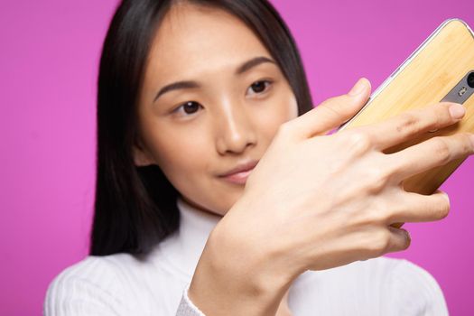 woman asian appearance phone in hands close-up technology gadget pink background. High quality photo