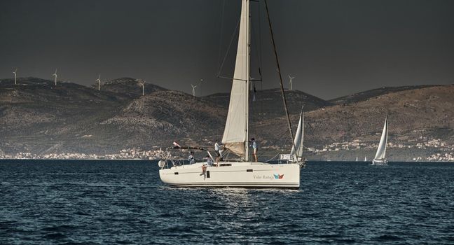 Croatia, Adriatic Sea, 15 September 2019: The race of sailboats, a regatta, reflection of sails on water, Intense competition, island with windmills are on background