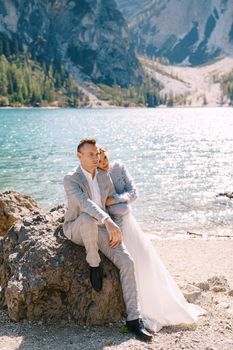 Bride and groom stand against the backdrop of stones overlooking the Lago di Braies in Italy. Destination wedding in Europe, on Braies lake. Loving newlyweds walk against backdrop of amazing nature