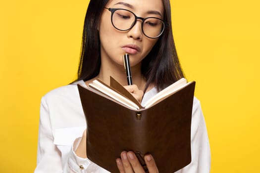 pretty brunette looking at notepad pen near lips elegant style yellow background. High quality photo