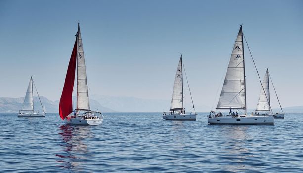 Croatia, Adriatic Sea, 15 September 2019: The race of sailboats, a regatta, reflection of sails on water, Intense competition, island with windmills are on background